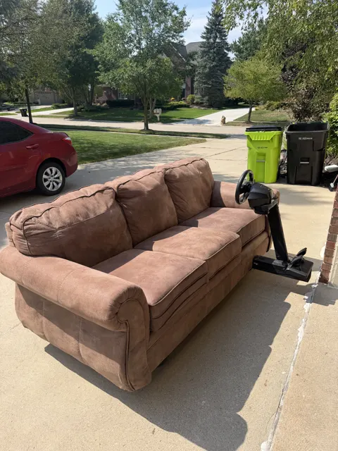 The couch on a driveway beside its wheel stand with the wheel and pedals